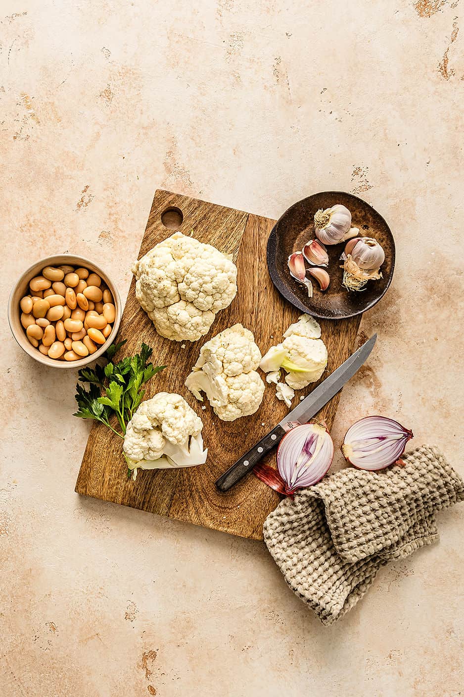 Overhead shot of cauliflower white bean soup ingredients including cauliflower, garlic, onion, parsley and beans.