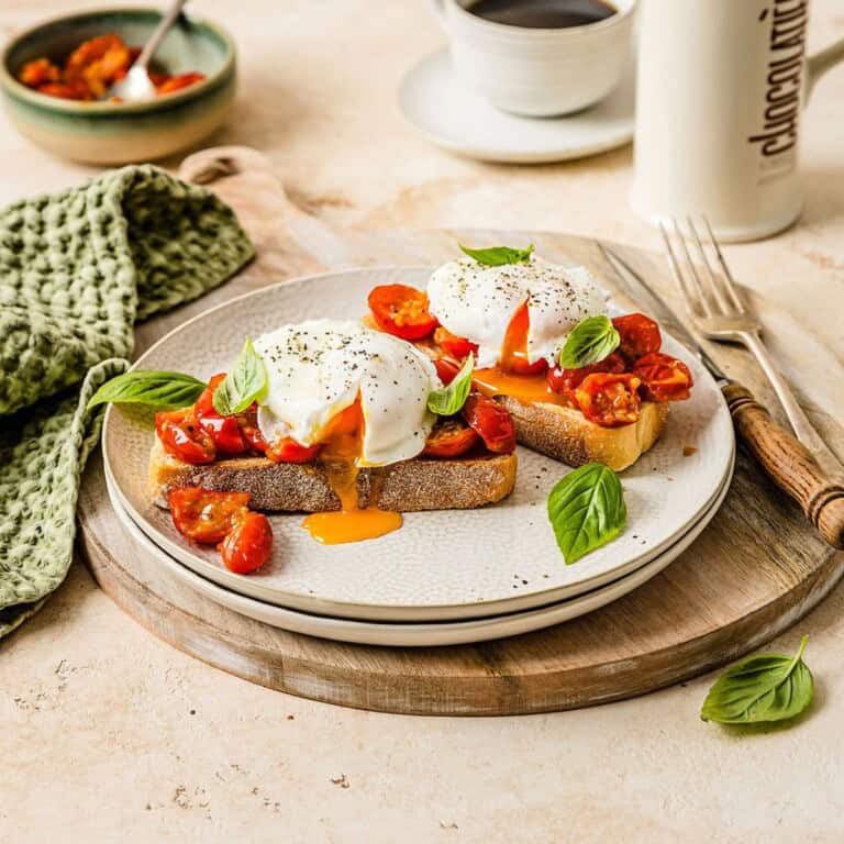Soft poached eggs on tomato bruschetta with fresh basil on a white plate, served with coffee. Perfect for a nutritious breakfast or brunch featuring simple, fresh ingredients.