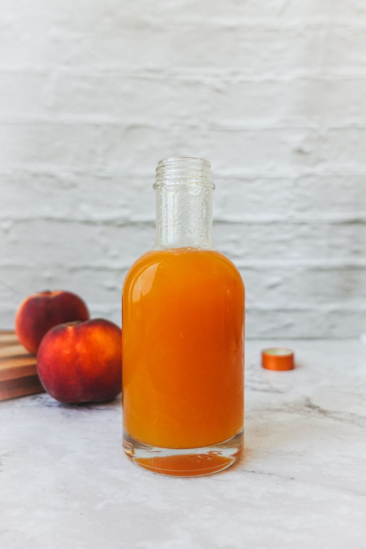 Straight-on shot of peach syrup in a glass bottle with peaches in the background.