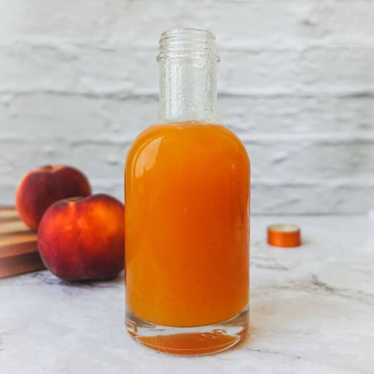 Fresh homemade peach juice in a glass bottle with ripe peaches in the background, perfect for healthy smoothies, breakfast, or refreshing summer drinks, emphasizing natural fruit juice recipes and fruity beverages.