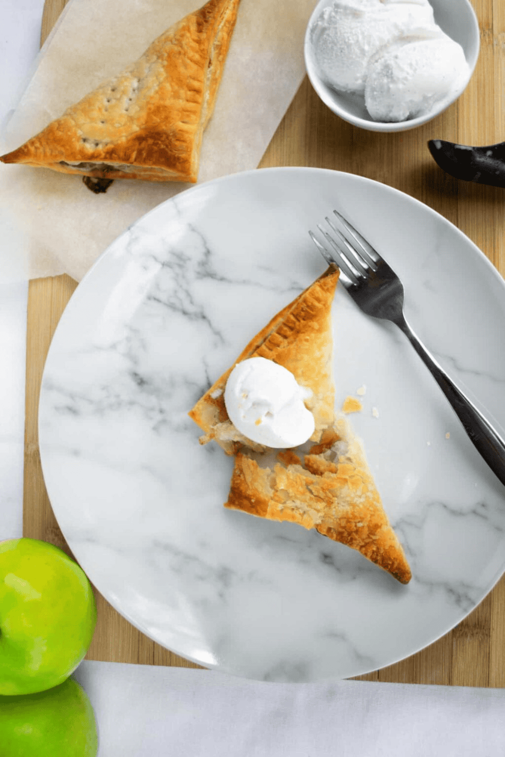 Golden apple hand pie with vanilla ice cream on marble plate, fresh green apple and scoop of ice cream, crispy flaky pastry dessert.