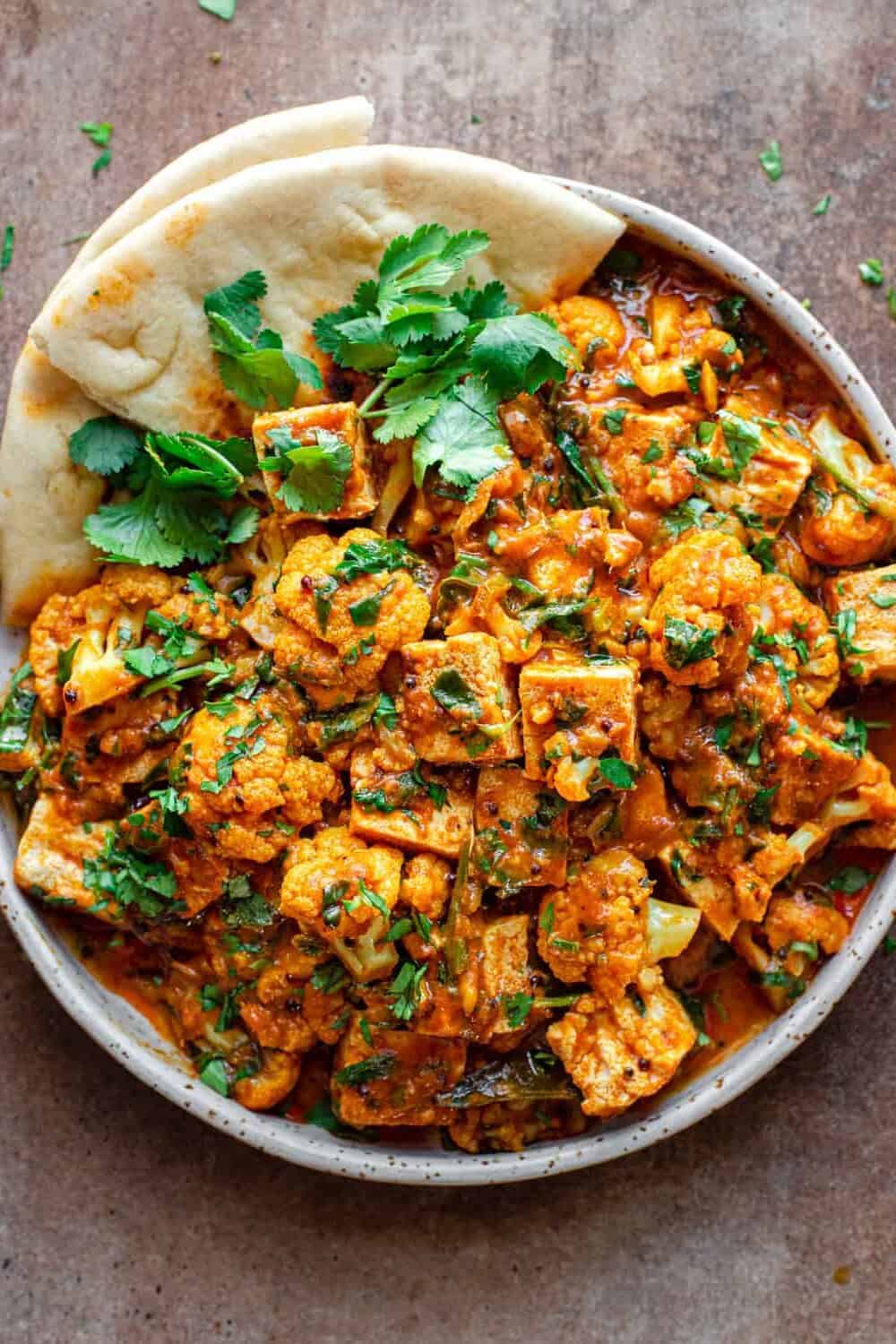 Overhead shot of tofu curry in a bowl with flatbread, topped with coriander.