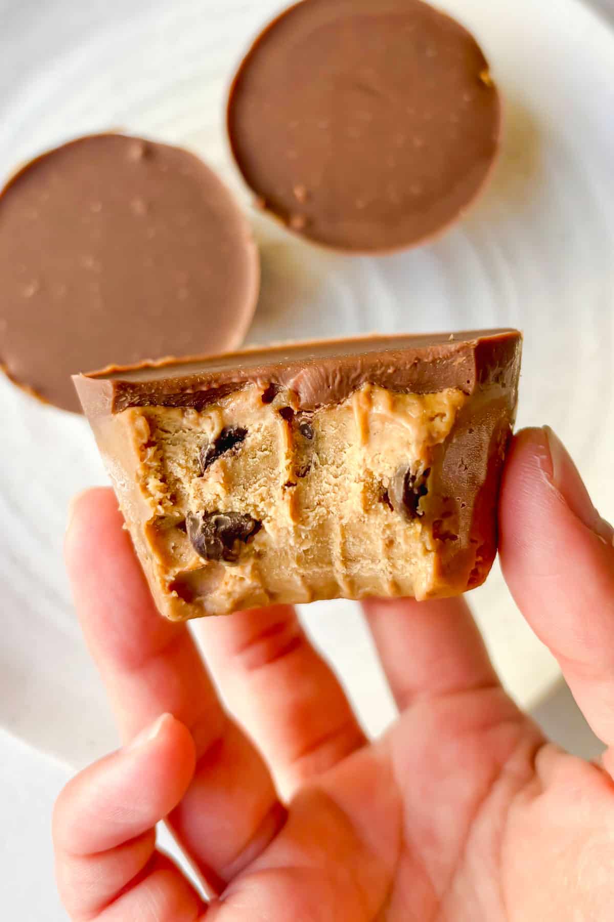 Front view of a cookie dough cup with a chocolate topping and a bite taken out of it.