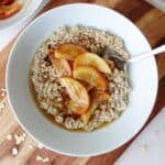 Creamy oatmeal topped with fresh sliced peaches and drizzled with honey, served in a white bowl on a wooden tray for a healthy breakfast.