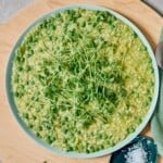 Creamy pea risotto garnished with microgreens, served on a white plate with a spoon and salt on the side, perfect for a healthy, flavorful meal.