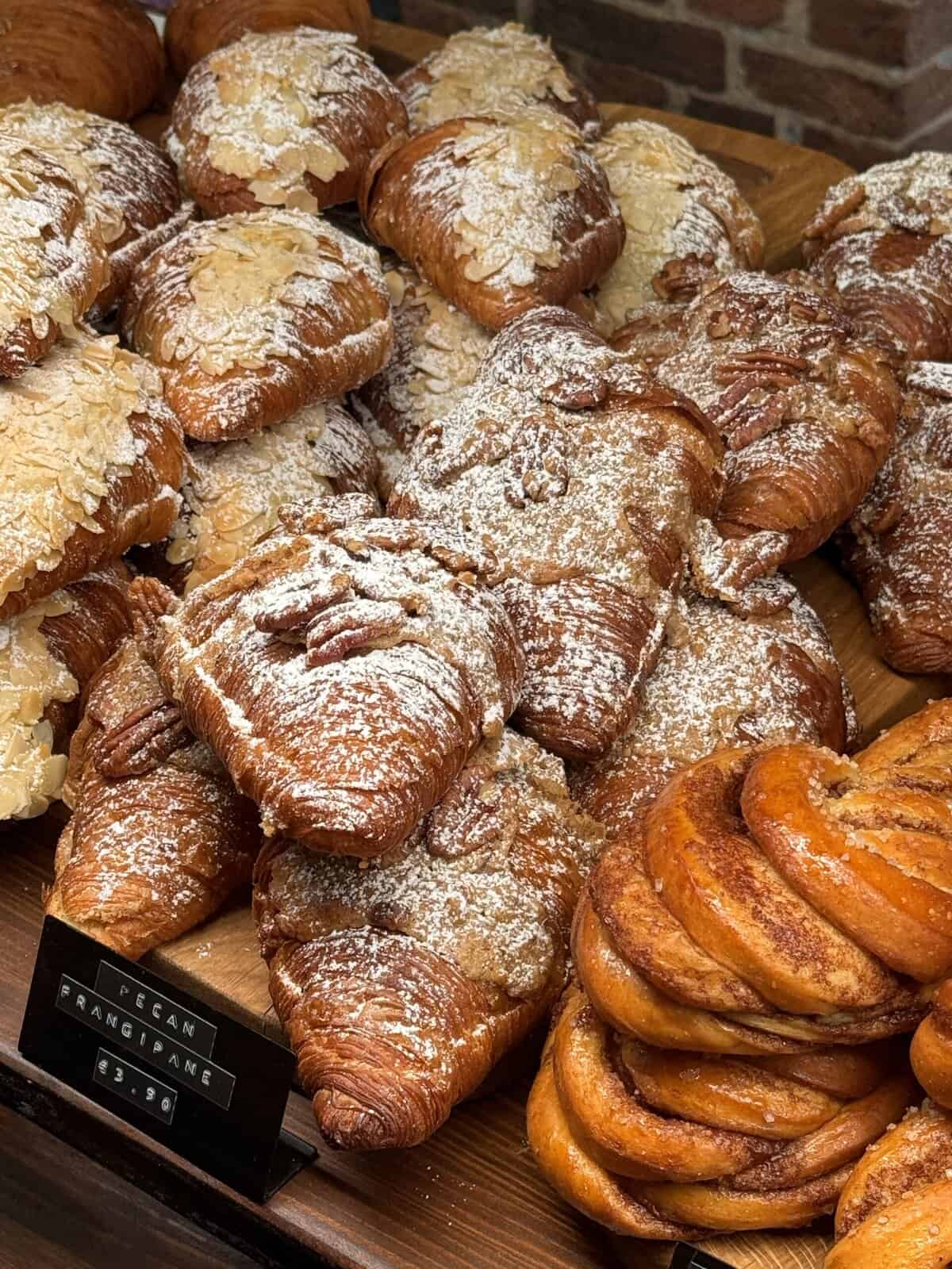Golden flaky croissants with almond topping and dusted powdered sugar in a bakery window.