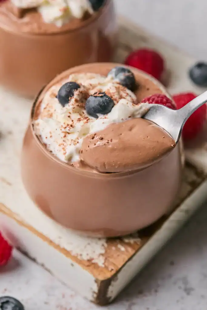 Chocolate pudding in a glass cup, topped with berries and whipped cream.