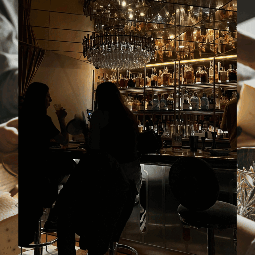 Luxury bar with illuminated shelves of whiskey bottles, elegant chandelier, and patrons enjoying drinks in a sophisticated setting.