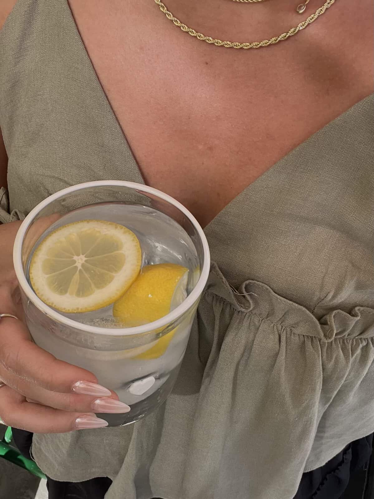 Woman holding a glass of soda water with lemon slices in it.