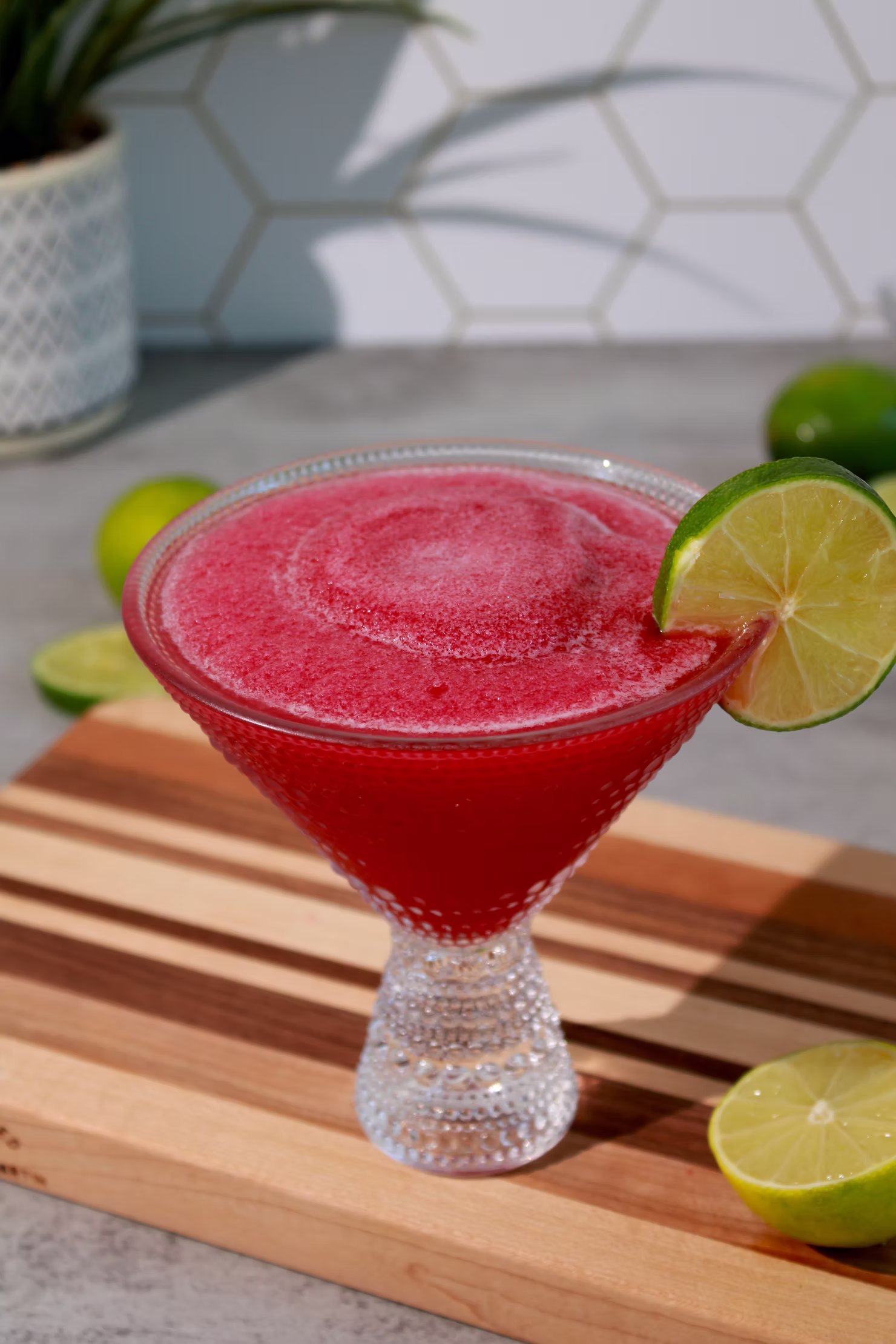 Frozen pomegranate margarita in a triangle-shaped glass with a lime wedge on the rim.