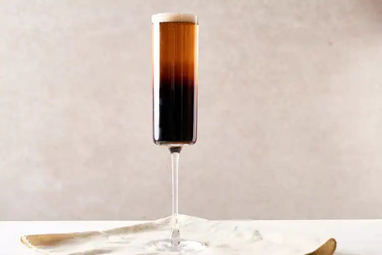 Black Velvet cocktail in a tall champagne flute against a beige background.