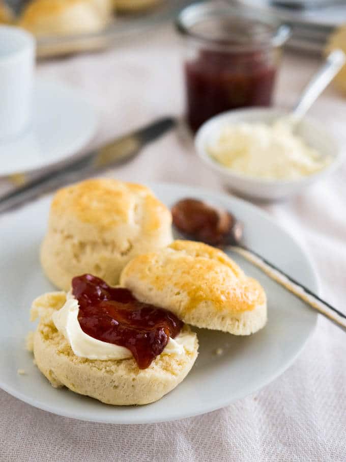 Homemade scones served with clotted cream and strawberry jam on a white plate.