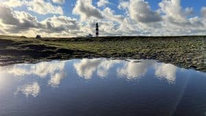 Coastal landscape with lighthouse reflected in water under cloudy sky