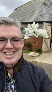 Man smiling outdoors in a garden setting with white blossom tree in the background