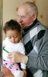 Elderly man reading with young child sitting on his lap at home