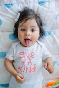 Smiling baby wearing &ldquo;one of a kind&rdquo; outfit lying on patterned blanket