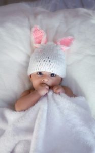 Baby wearing knitted bunny hat wrapped in white blanket