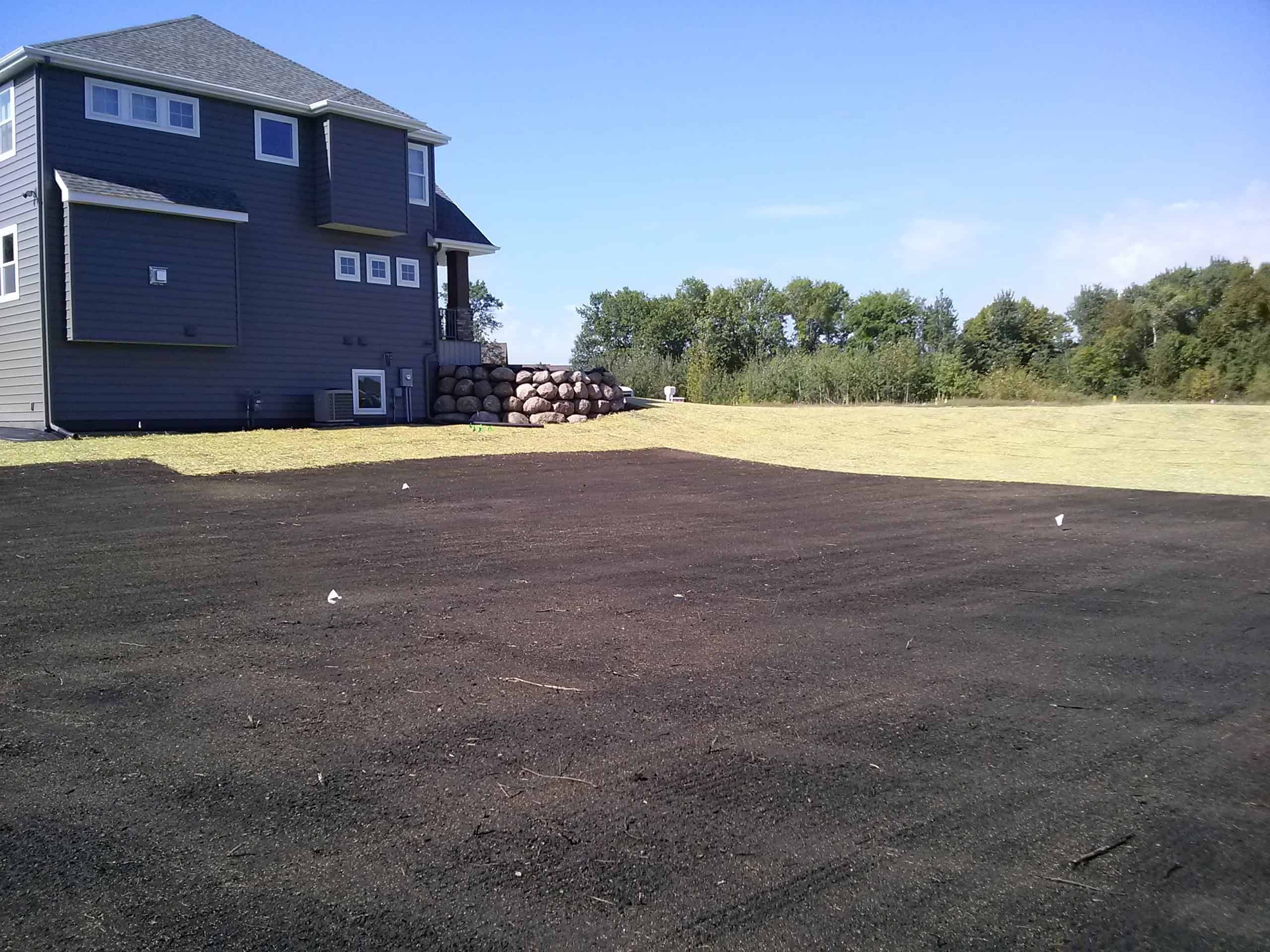 Freshly landscaped lawn in backyard with black topsoil and green grass near modern house.