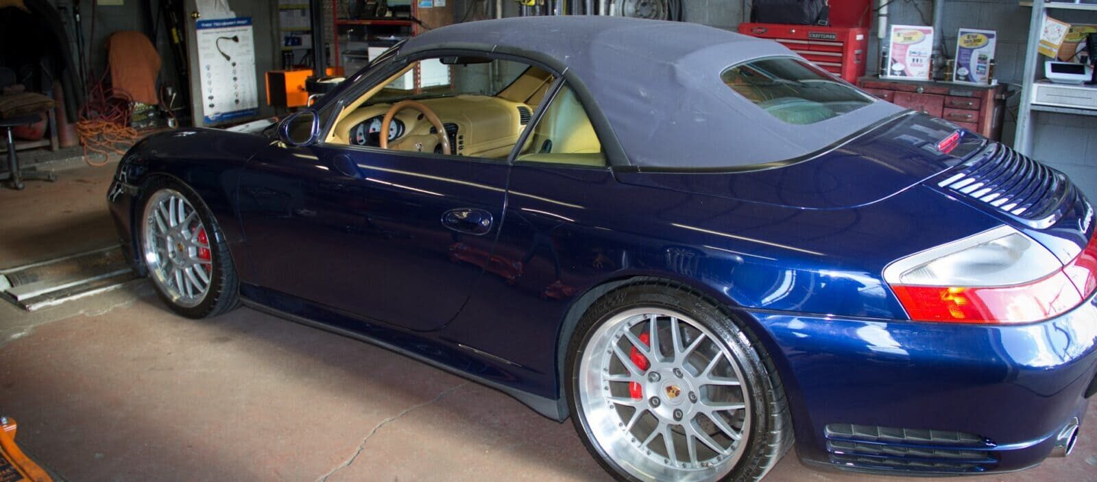 Blue Porsche convertible car parked indoors at auto repair shop.