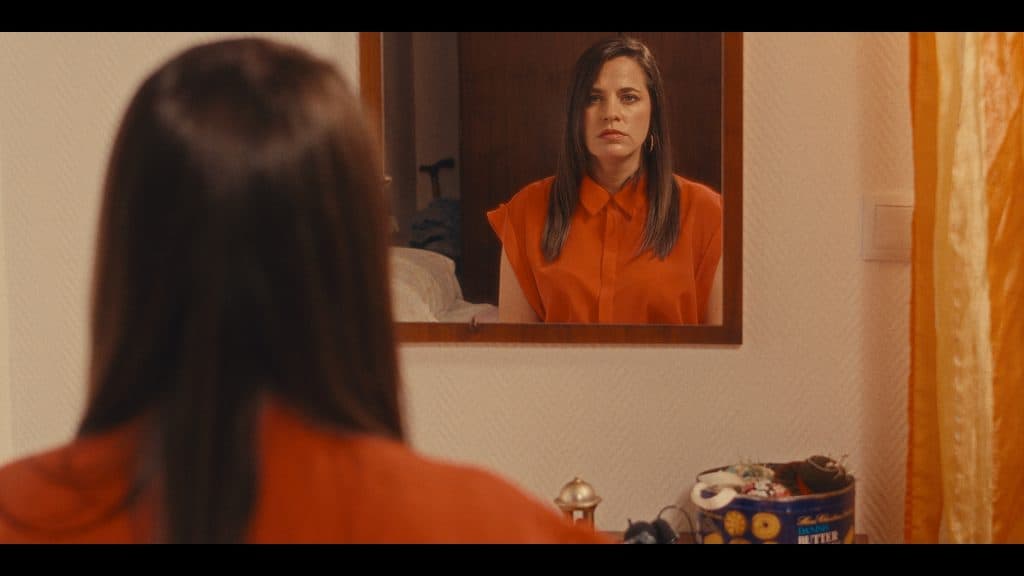 Reflejo de una mujer observándose en un espejo, destacando una escena introspectiva y emocional en un ambiente hogareño, con énfasis en la moda y el estilo personal.