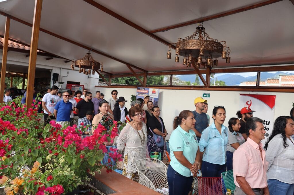 1. Personas reunidas en evento público en Huila, Colombia, durante una ceremonia o reunión comunitaria, con un ambiente al aire libre y decoración floral en un espacio cubierto.