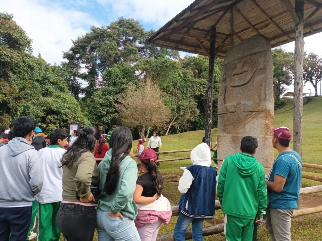 1. Personas observando una escultura precolombina en un parque natural en Huila, Colombia, con paisaje verde y árboles, promoviendo turismo cultural y arqueológico en la región.