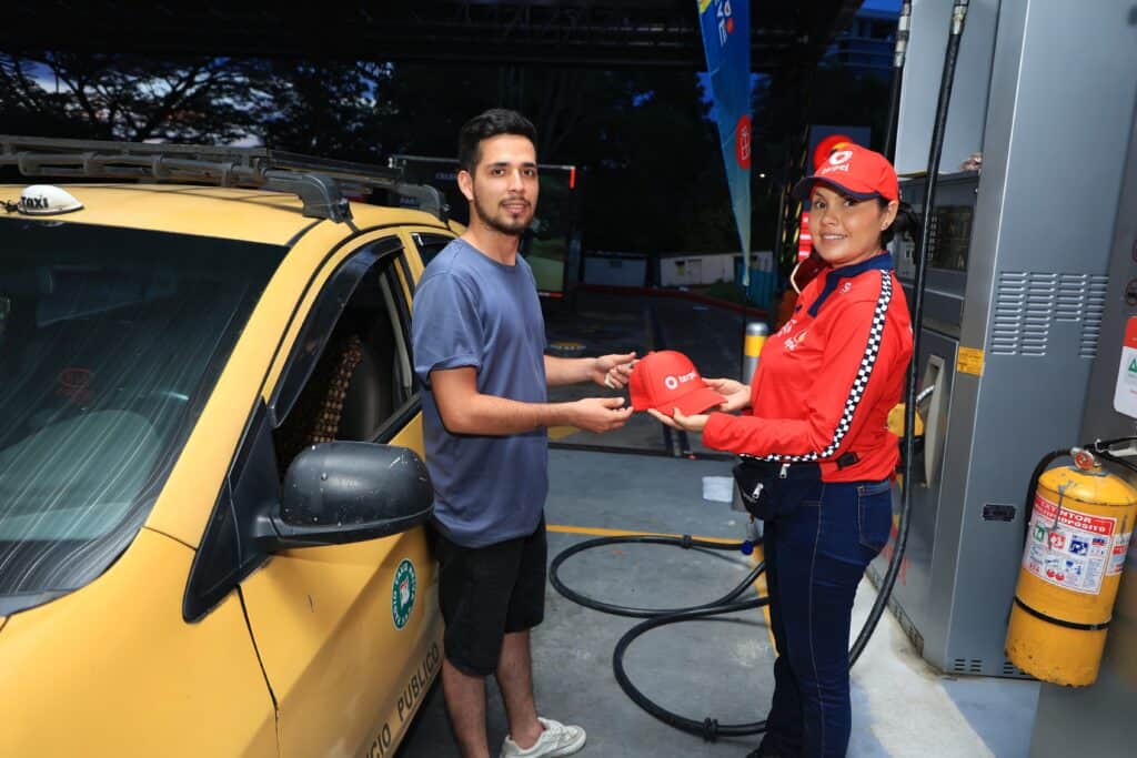 Hombre recibiendo un sombrero de una empleada en una estación de carga de vehículos eléctricos, promoviendo energía limpia en Huila.