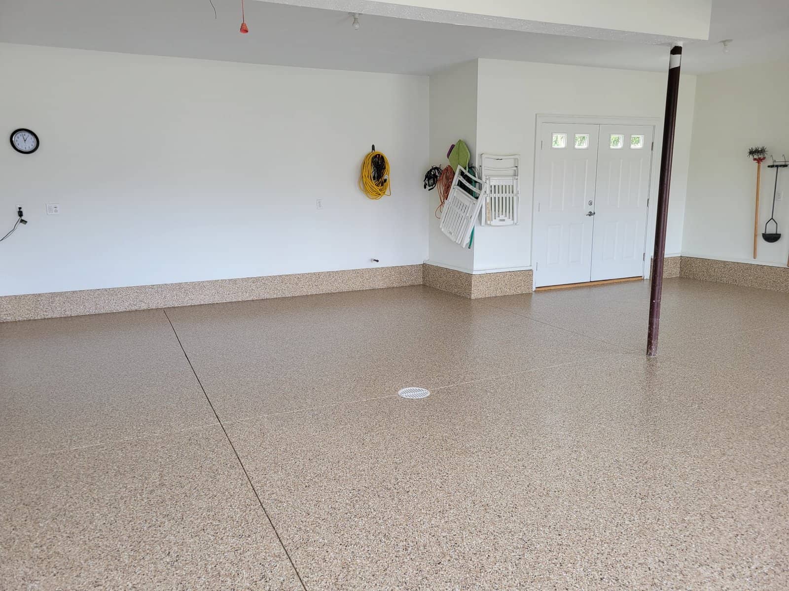 The garage shows a smooth, shiny floor by J&P Coatings. It looks neat and ready for use, with only a few tools and chairs stored inside.