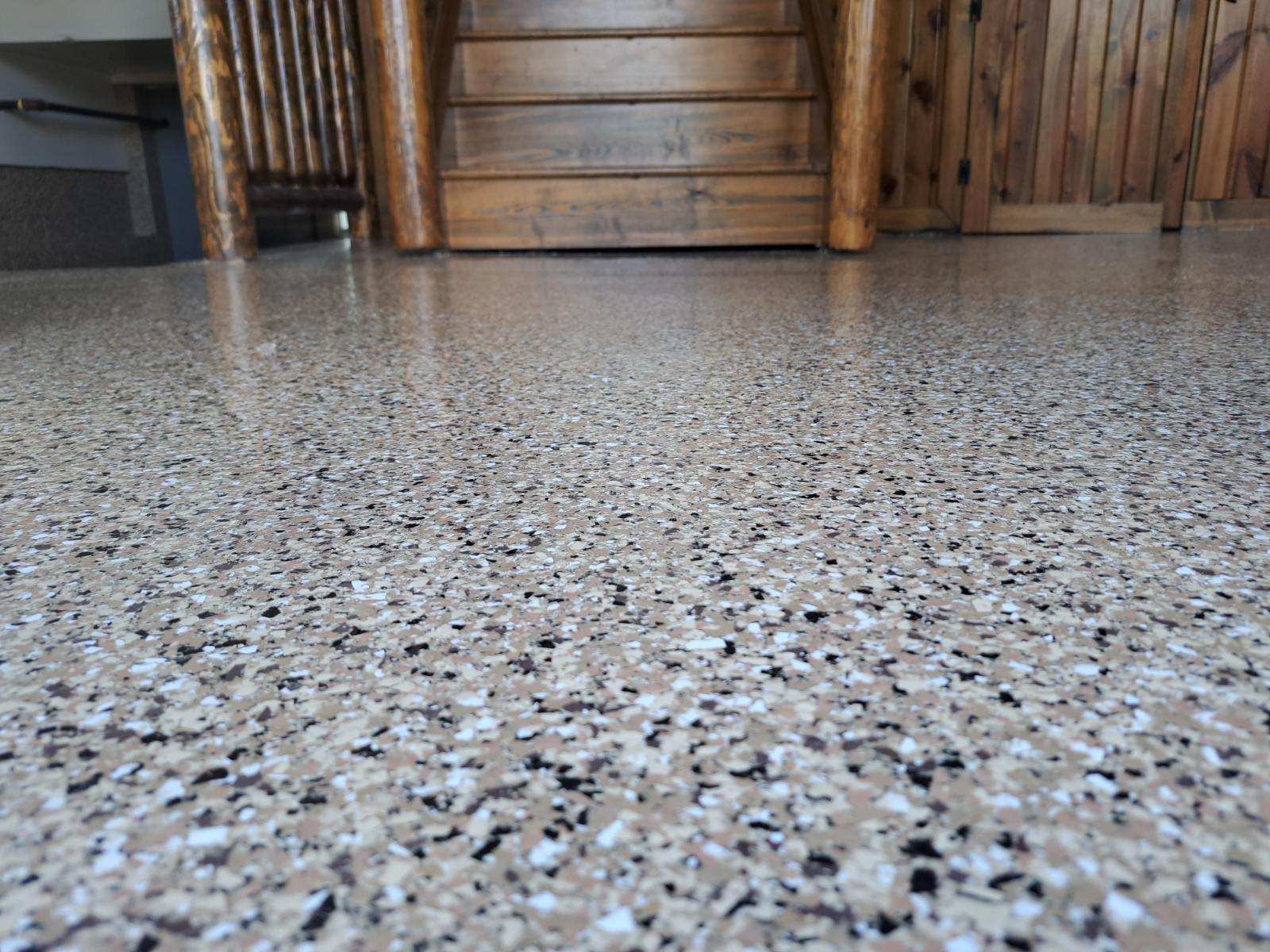 This image shows a smooth, speckled epoxy floor by J&P Coatings. It gives an idea of how your basement or patio can look after getting professional concrete coating. Wooden stairs hint that it works well indoors too.