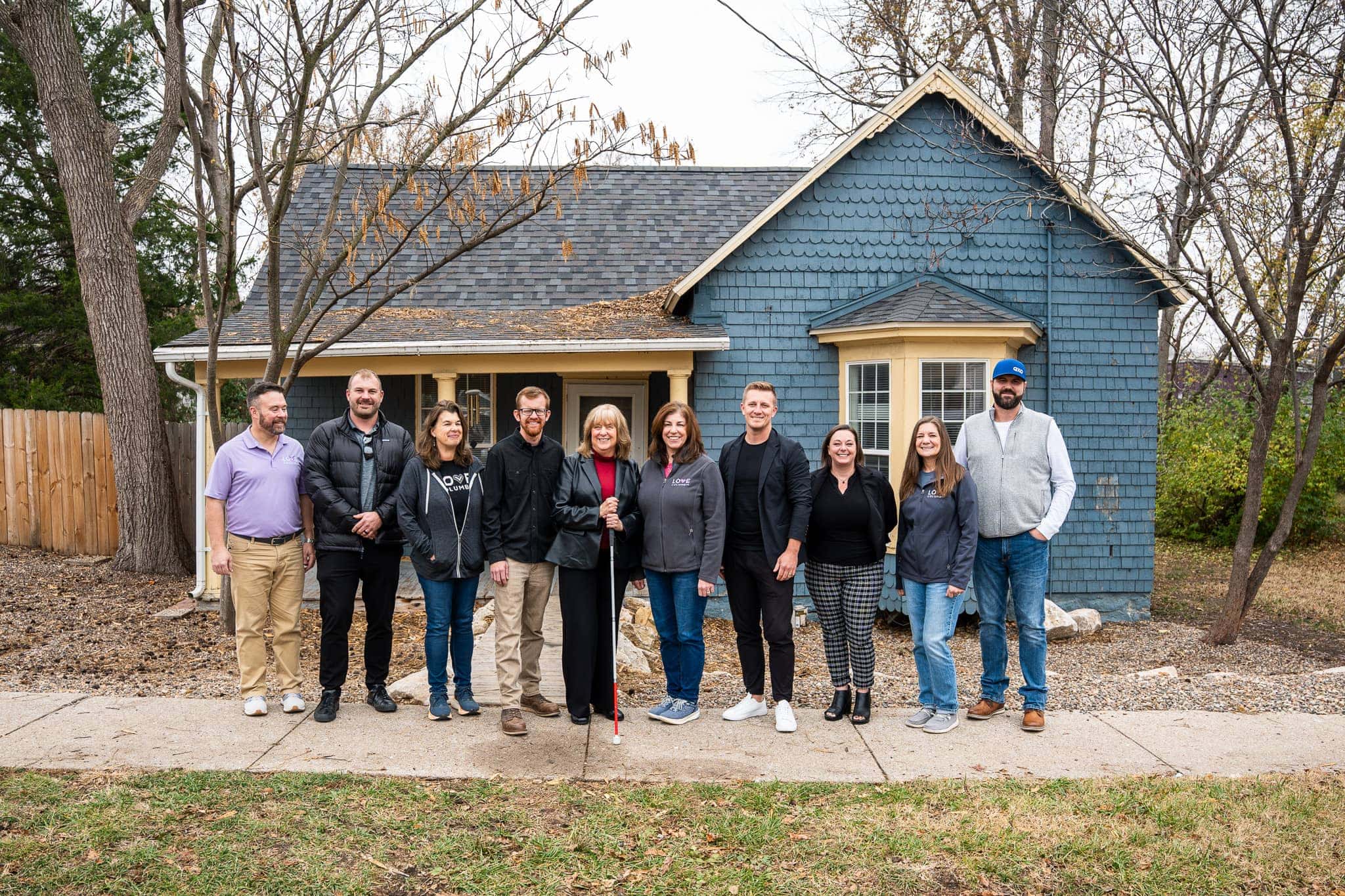Roofing professionals standing in front of a freshly roofed blue house with a team of experts in Midwest roofing.