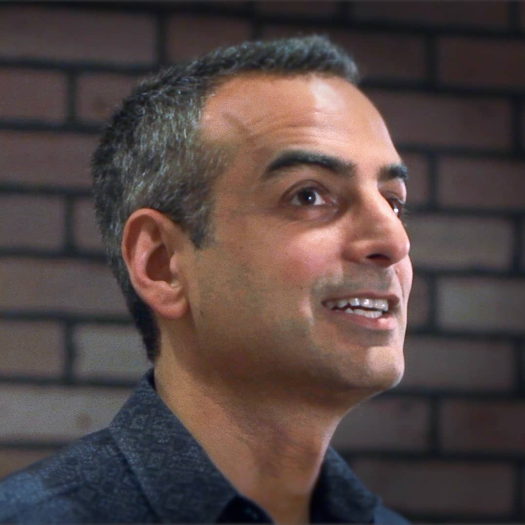 A smiling middle-aged man with gray hair, wearing a blue shirt, looking slightly upwards, with a blurred brick wall background titled "Generation Freedom.