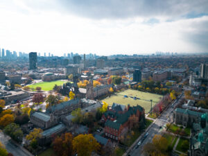Aerial view of cityscape with historic and modern buildings, autumn foliage, and a cloudy sky.
