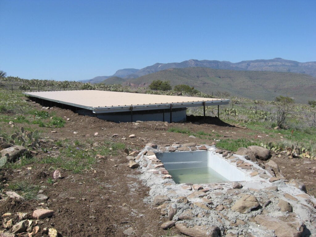 Natural desert landscape with water source and mountain views, supporting bighorn sheep populations.