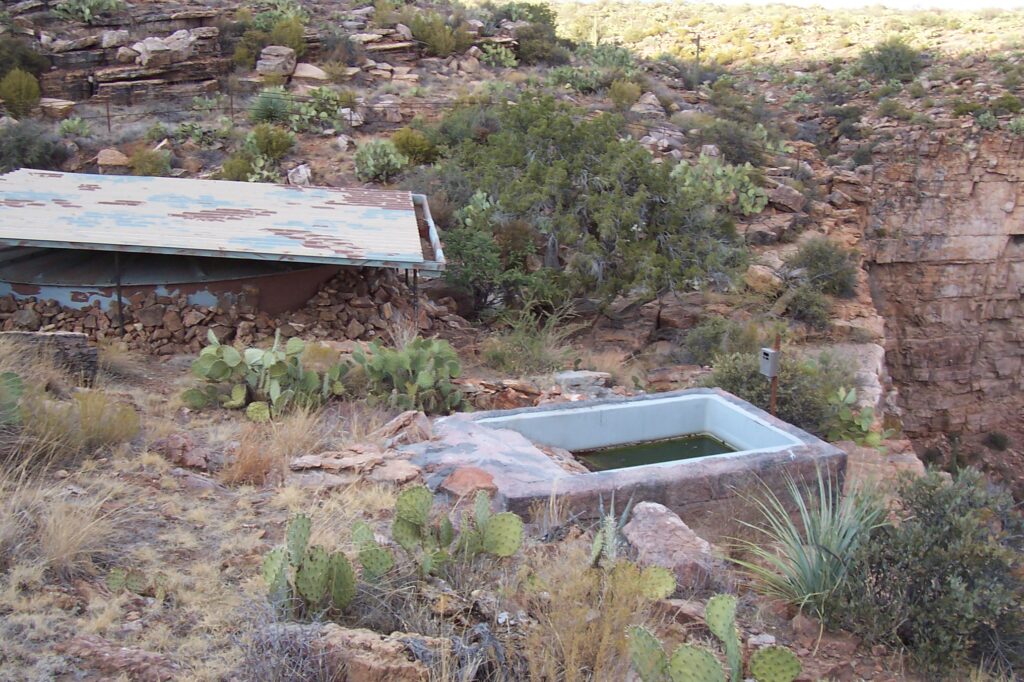 Desert landscape in Mesa, Arizona, featuring a water trough, cacti, and rugged rocky terrain.