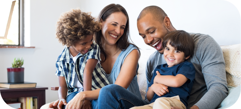 A family of four, two adults and two children, sit closely together on a couch, smiling and laughing in a well-lit room. Their joy is palpable, much like the satisfaction brought by advanced services that enhance everyday experiences.