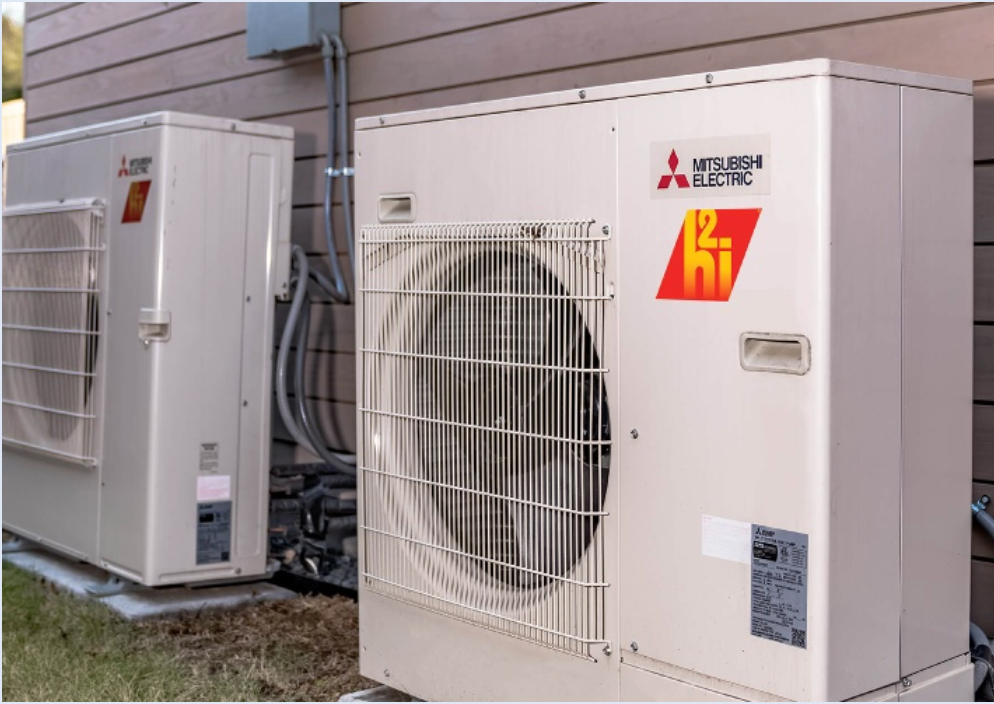 Two Mitsubishi Electric products, both outdoor air conditioning units, are installed side by side against a wooden wall. They feature large fans and branded logos on their casings, providing efficient cooling with sleek design.