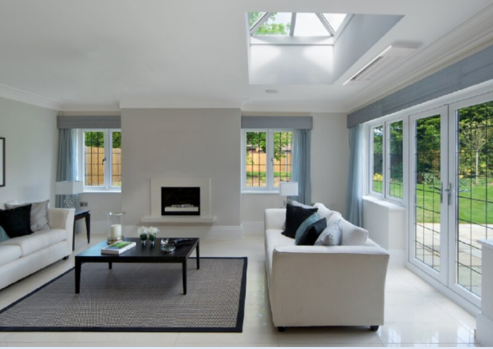A modern living room features products such as two white sofas and a sleek black coffee table. A cozy fireplace and large windows overlooking a lush garden enhance the ambiance, while a skylight floods the space with natural light.