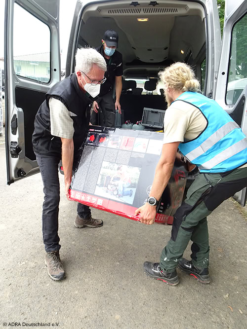 1. Mehrere Helfer beim Ausladen einer großen Spendenbox aus einem Transporter, Helfer tragen Masken, Einsatz für Wohltätigkeit und Gemeinschaft.