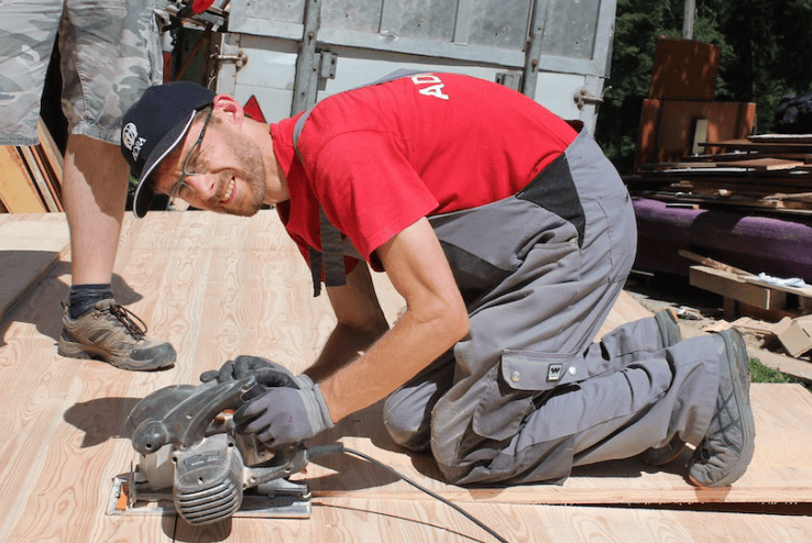 Schreiner arbeitet mit einer Kreissäge auf einer Holzbohle auf einer Baustelle, professionelle Handwerksarbeit im Holzbau, Handwerker bei der Holzbearbeitung, Qualität in der Holzverarbeitung.