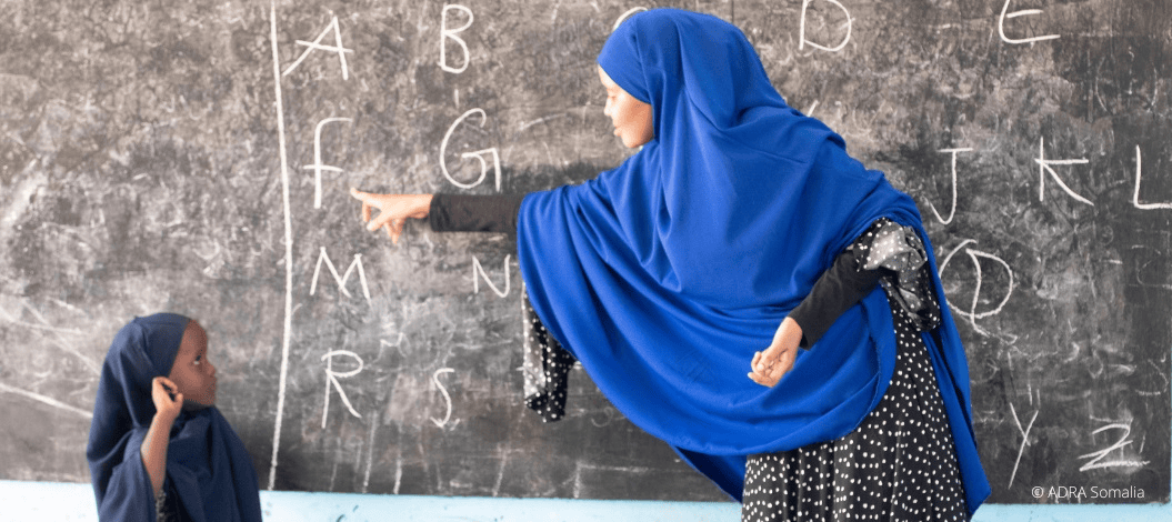 Lernende Frau mit Kopftuch unterrichtet Kinder an der Tafel, symbolisiert Bildung und religiöse Werte, passend zu advent-verlag.de für christliche Bildungs- und Religionsmaterialien.