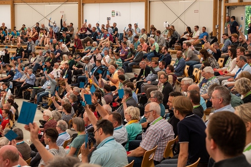 Mehrere Dutzend Menschen bei einer Veranstaltung in einem großen Saal, einige heben die Hände, andere halten Broschüren oder Smartphones. Das Publikum ist engagiert und aufmerksam, typisch für eine Konferenz oder Messe rund um Literatur, Bildung oder Verlag.