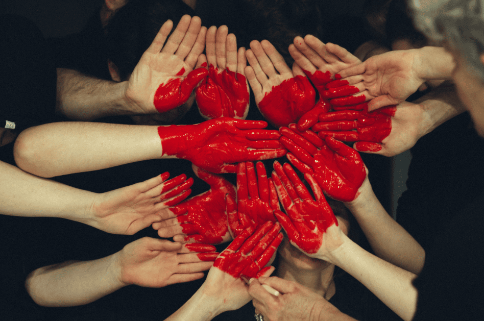 Freiwilligenarbeit und Gemeinschaft: Menschen mit roten Fingerfarben bilden ein Herz aus Händen, symbolisierende Zusammenarbeit und Solidarität für soziale Projekte und Engagement.