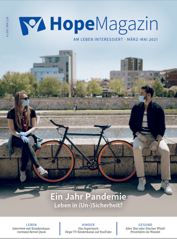 Stressfreies Fahrrad und zwei Menschen, die soziale Distanz mit Masken wahren, auf einem Flussufer in einer Stadt.