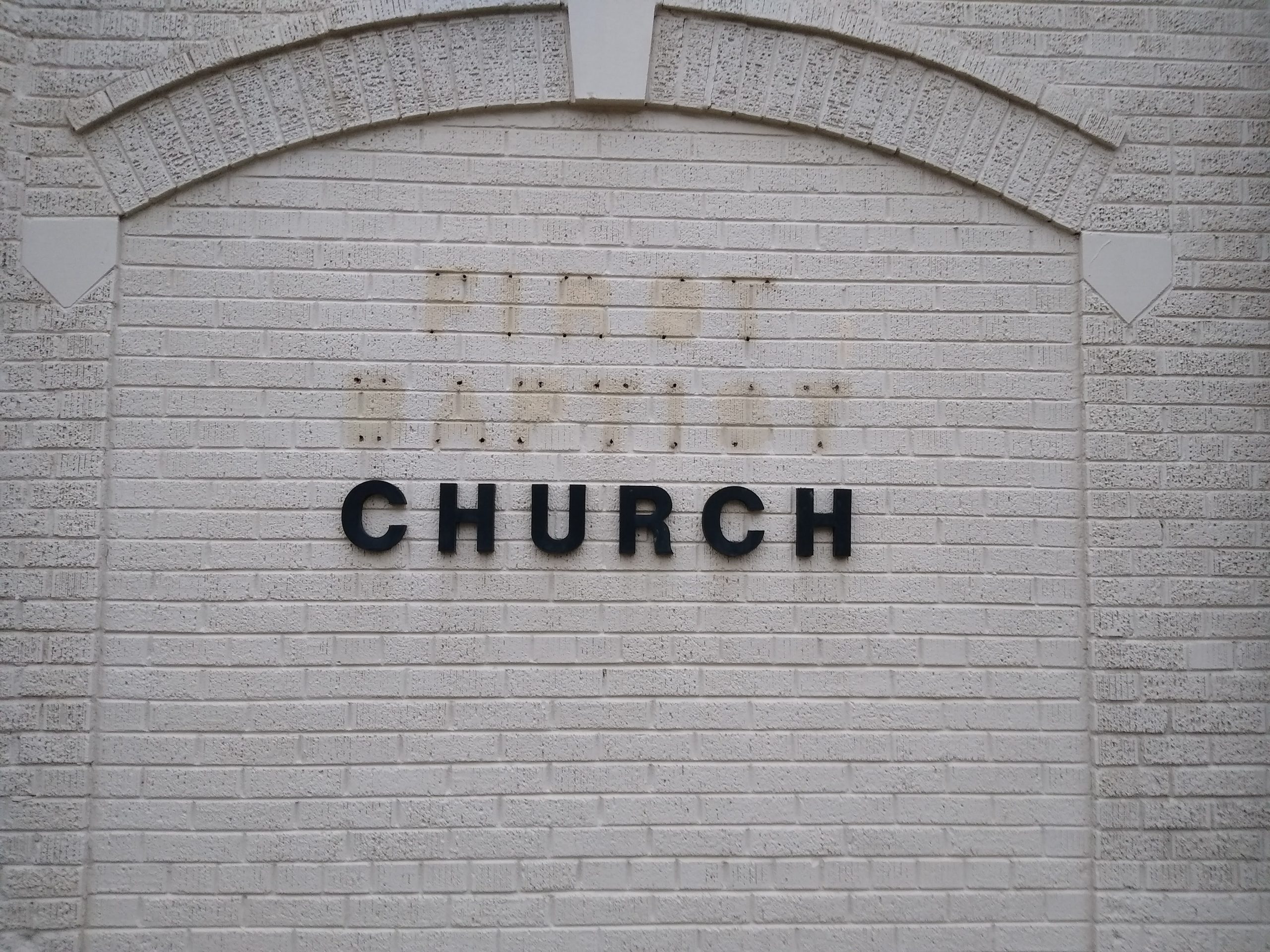 Helle weiße Backsteinmauer mit dem schwarzen Schriftzug „CHURCH“ und Platz für ein späteres Kirchenlogo oder Namensschild. Perfekt für kirchliche Einrichtungen, mit klarer, moderner Ästhetik.