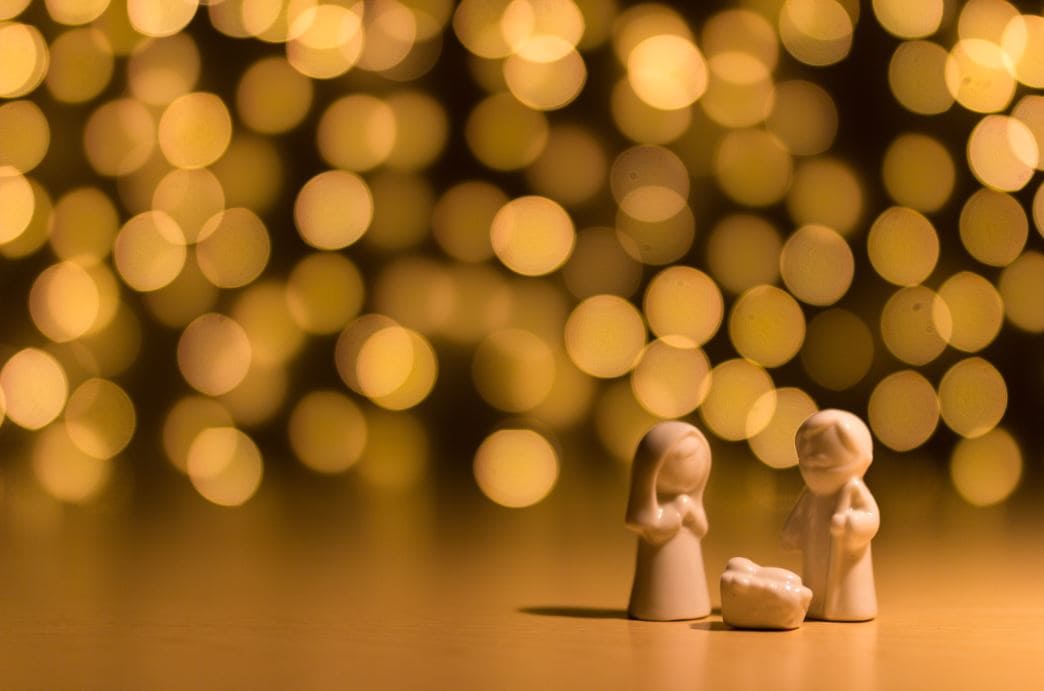 Kleines Krippenset mit Maria, Josef und Jesusfigur vor einem warm beleuchteten Bokeh-Hintergrund, ideal für Advents- und Weihnachtsdekorationen.