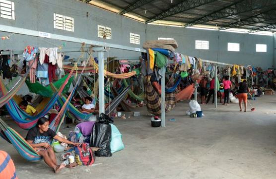 Menschen in einer Flüchtlingsunterkunft mit Hängematten und persönlichen Gegenständen, symbolisch für Flüchtlingshilfe und humanitäre Unterstützung.