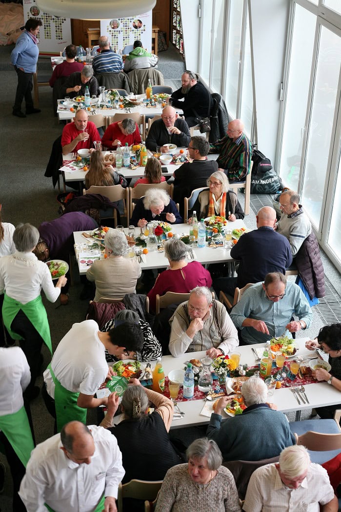 Gemütliches Gemeinschaftsessen bei Advent-Verlag mit vielfältigen Speisen, fröhlichen Menschen und festlicher Atmosphäre, perfekt für Familien und Freunde.