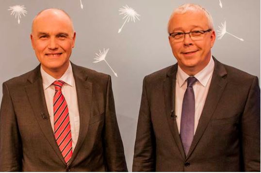 Hochwertiges Bild von zwei professionellen Männern in Anzügen bei einer Veranstaltung, Fokus auf Geschäft, Kommunikation und Zusammenarbeit.
