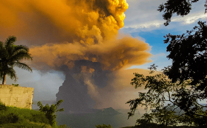 1. Großbildaufnahme eines Vulkans mit aufsteigendem Rauch und Lava bei Sonnenuntergang, umgeben von Natur und Bäumen, symbolisiert Naturkraft und Naturschauspiele.