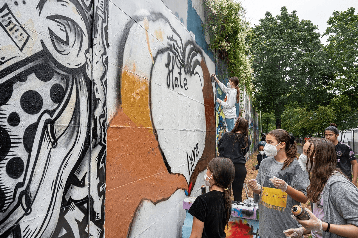 Kreatives Graffiti-Kunstprojekt an einer Wand in Berlin, Jugendliche beim gemeinsamen Graffiti-Sprayen, soziale Kunstaktion, Street Art, urbanes Engagement, Graffiti-Workshop, Gemeinschaft, Urban Art, Jugendkultur, Kunst im öffentlichen Raum.